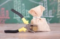 A sack of funds and a pair of pliers holding a euro coin in front of a blackboard with financial graphics