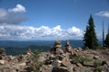 Sacred cairns next to tall pine trees on top of a mountain overlooking a valley under a blue cloudy sky