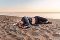 Young sad abandoned woman lies on a sandy beach with a sunset on the background Royalty Free Stock Photo