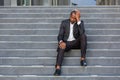 Sad african american businessman sitting on stairs outside office building, man in business suit bankrupt fired from job Royalty Free Stock Photo