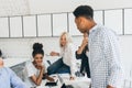 Sad african girl sitting in office with pen and notebook while her european colleagues trying to help her to figure out