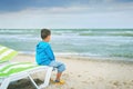 Sad alone kid sitting on beach, looking at sea and thinking. The end of summer. sadness about end of vacation Royalty Free Stock Photo