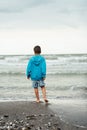 Sad alone kid standing on beach, looking at sea and thinking. Royalty Free Stock Photo