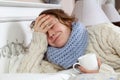 Sad alone young woman in white sweater and blue scarf feeling headache and cold sick and resting home in bed. holding her painful Royalty Free Stock Photo