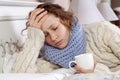 Sad alone young woman in white sweater and blue scarf feeling headache, cold sick and resting home in bed. holding her painful Royalty Free Stock Photo