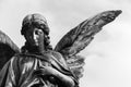 Sad angel sculpture with open long wings across the frame against a bright white sky. The sad expression sculpture in BW.