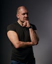 Sad angry crime man with bald head thinking with doubt look in agressive black shirt on dark grey background. Closeup