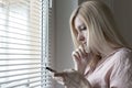 Sad apathetic lonely woman standing near the window and texting messages in smartphone at home or hotel, divorce, depression and Royalty Free Stock Photo