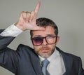 Sad and ashamed businessman in weird broken glasses doing L loser sign with hand and fingers on forehead with funny depressed Royalty Free Stock Photo