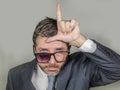 Sad and ashamed businessman in weird broken glasses doing L loser sign with hand and fingers on forehead with funny depressed Royalty Free Stock Photo