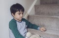 Sad asian boy wearing pyjamas sitting at carpet staircase in the morning, Lonely kid looking dow with sad face, Depressed child