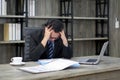 Sad Asian businessman holds his temple with both hands, sitting in the office. The concept of unemployed, sadness, depressed and