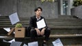 A sad Asian businessman sits on the stairs with a box of his personal stuff after losing his job Royalty Free Stock Photo