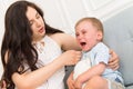Sad baby crying near woman - tantrum child with mother on sofa