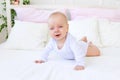 Sad baby girl 6 months old in a white bodysuit lying on her stomach on a white bed at home Royalty Free Stock Photo