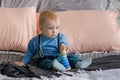 Sad, but beautiful blue-eyed baby sitting on the bed next to the toy pyramid Royalty Free Stock Photo