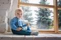 Sad, but beautiful blue-eyed baby sitting on the windowsill and looking at the camera Royalty Free Stock Photo