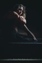 Sad beautiful girl sitting on black piano in the dark room