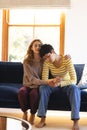 Sad biracial lesbian couple embracing and comforting, on couch in sunny living room, copy space