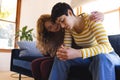 Sad biracial lesbian couple embracing and comforting, sitting on couch in sunny living room