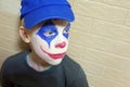 A sad blue-eyed boy in a blue cap with a clown mask painted on his face looks to the side. Body painting and makeup celebration Royalty Free Stock Photo