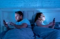 Sad and bored couple addicted to smart mobile phones late at night in phase of mutual disinterest