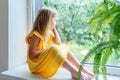 Sad bored little girl on windowsill looking out window on rainy summer day Royalty Free Stock Photo