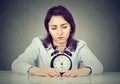 Sad bored woman with alarm clock sitting at table in her office Royalty Free Stock Photo