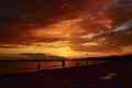 Sad boy on the bridge stands under sky and reflective water surface. Lonely man silhouette watches red cloudy sunset above lake at Royalty Free Stock Photo