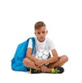 A sad boy isolated on a white background. Tired kid with a bright satchel and a soccer ball. A sitting child. Copy space Royalty Free Stock Photo