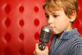 Sad boy with microphone on rack against red wall Royalty Free Stock Photo