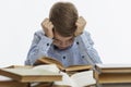 Sad boy sits at a table with many books. A child of 9-10 years old in a blue shirt clasped his head in his hands. White background Royalty Free Stock Photo