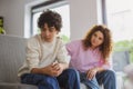 Sad boy sitting on sofa in living room with his mother in background Royalty Free Stock Photo