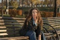 Sad brooding girl with long brown hair sits on bench in autumn park and thinks about something. Beautiful young woman Royalty Free Stock Photo