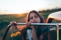 Sad brunette teen girl with sunflower in hand leaned on the car door and looking away, sunset on the background Royalty Free Stock Photo