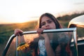 Sad brunette teen girl with sunflower in hand leaned on the car door and looking at the camera, sunset on the background Royalty Free Stock Photo