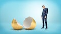 A sad businessman on blue background looks down on a giant broken golden egg. Royalty Free Stock Photo