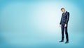 A sad businessman standing on blue background looking down with slumped shoulders. Royalty Free Stock Photo