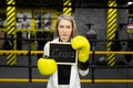 Sad businesswoman in a suit in a boxing ring wearing gloves holds a sign that says crisis.