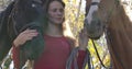 Sad Caucasian woman with problem skin holding bridles of two horses outdoors. Sick woman undergoing hippotherapy in