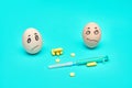 Sad chicken eggs medical syringe and pills on a blue background. health concept