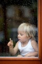 Sad child behind the window on rainy day