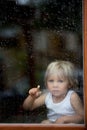 Sad child behind the window on rainy day