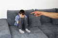 Sad child, a boy sitting on a gray sofa in the room and covered his face with his hands, the hand of the parent accusing finger Royalty Free Stock Photo