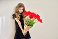 Sad child girl with a bouquet of red tulips in black dress