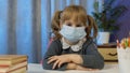 Sad child girl pupil in medical mask doing school homework at home, video call by webcam on internet Royalty Free Stock Photo