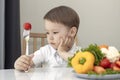 a sad child holds a tomato on a fork, an unhappy little boy eat vegetables Royalty Free Stock Photo