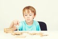 Sad child sitting at table. Child plays with construction toy blocks at the table. Sad bored boy build wooden house. Kid plays wit Royalty Free Stock Photo