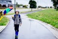 Sad child walking in rubber wellingtons on wet footpath.