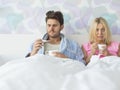 Sad couple holding coffee mugs while relaxing on bed Royalty Free Stock Photo